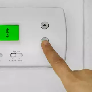 Someone pressing a button on an HVAC thermostat that registers $