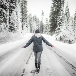 An icy winterscape, a woman walking down the center of a road, the world and trees covered in ice.