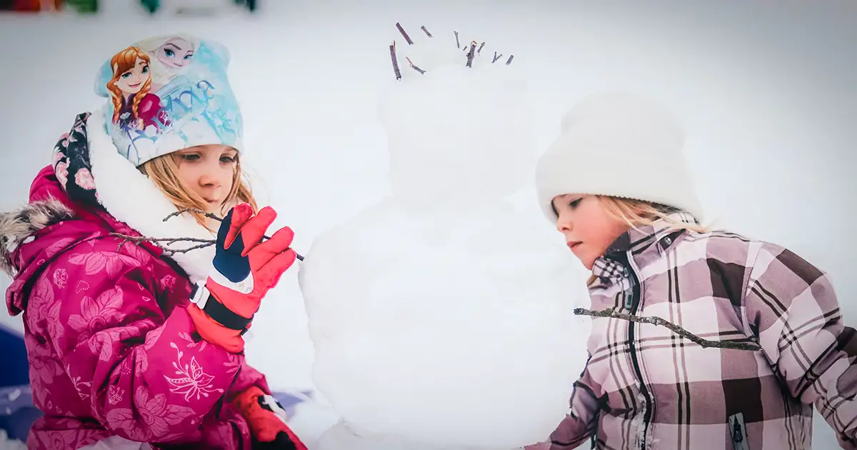 Two young children building a snowman.