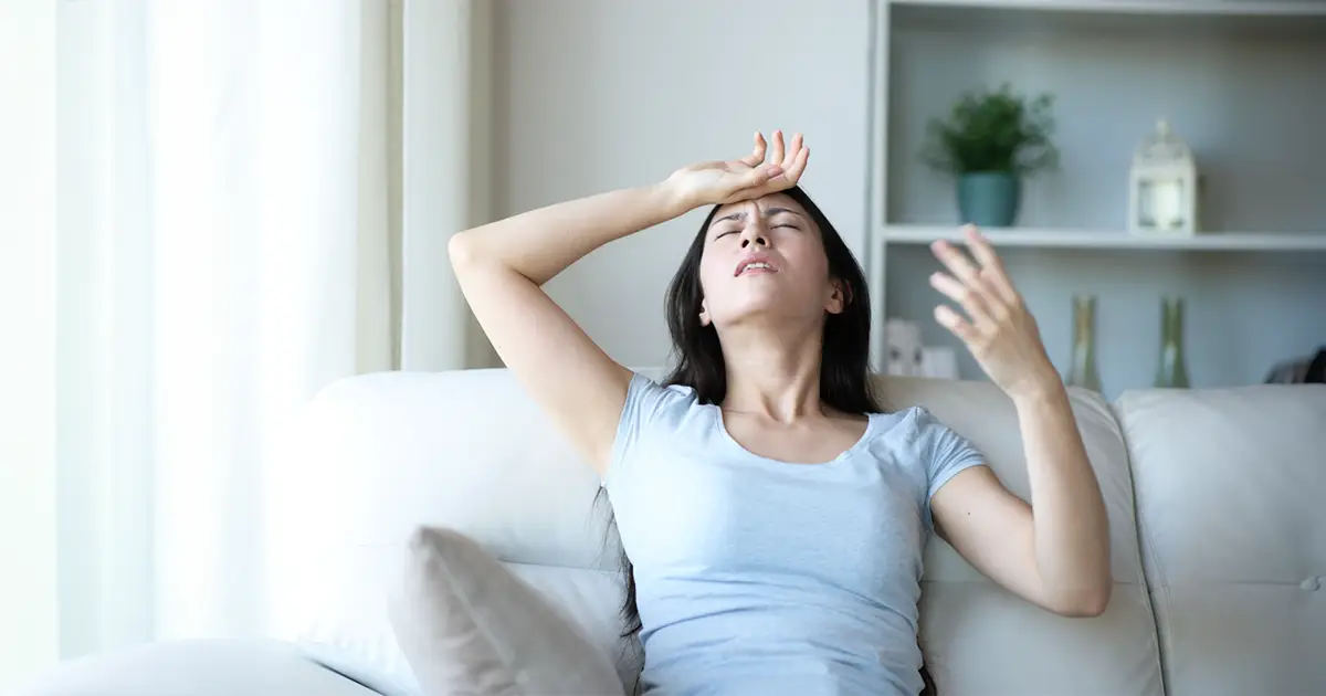 A woman sits on her couch, hot and upset over increased AC repair bills.
